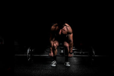 A lean, focused lifter training in a dark, minimal gym